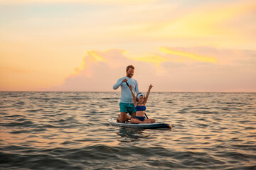 Instructor and pre-school girl to surfing on a sup board. Sea and the sunset in the background....