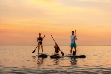 Group of caucasian people swimming on a sup boards at the ocean. Sport activity of friends at the...