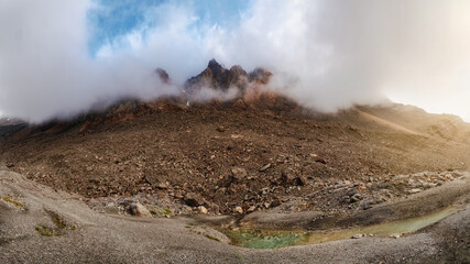 Atmospheric morning mountain landscape. Panoramic landscape in highlands. Sharp peaks of the rocks look out from the clouds and morning fog.