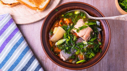 Rustic soup with trout and vegetables in a plate, top view on a table with toast
