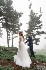 bride and groom hold hands and go in a mysterious misty mountain forest. trust