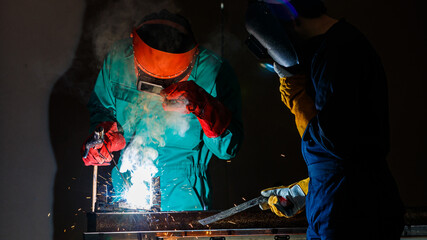 a factory worker wearing a green mechanic coveralls and safety helmet welding metalwork at night...