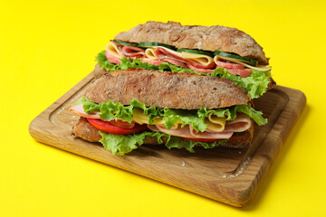 Board with ciabatta sandwiches on yellow background