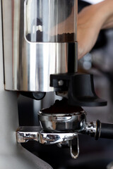 close up photo of male hands holding a metal tamper and a portafilter with coffee in a coffee shop. A man barista preparing for pressing ground coffee for brewing espresso or americano in a cafe.