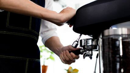 Image is portrait. Asian young man smile using a coffee machine. Rinse the coffee with warm water. Asia man preparing for pressing ground coffee for brewing espresso or americano in a cafe.