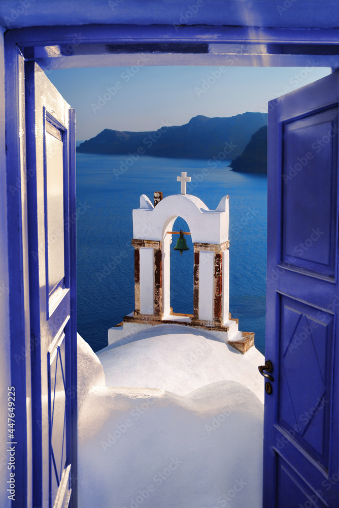 Wall mural santorini view with bell against open blue door in oia village, greece