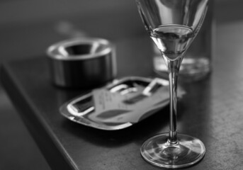 Glass of wine, ashtray and restaurant bills on a table. Black and white photo.