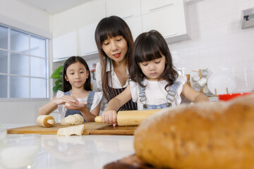 A cute Asian mother teaching the two little daughters, 3 years and 7 years old, how to mak bread and bakery in modern kitchen. Idea for love and relationship in family