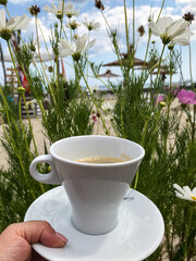 a cup of coffee in a woman's hand on a background of flowers. sky and sea