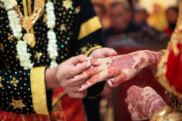Young Asian muslim couple holding hand and putting wedding ring each other in a traditional minangkabau culture ceremony. Henna tattoo on bride hands.