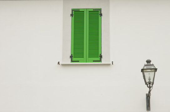 Detail of a green window and old street lamp against the background of a white wall