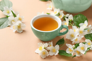 Fototapeta na wymiar Cup of jasmine tea and flowers on color background