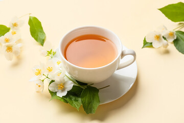 Cup of jasmine tea and flowers on color background
