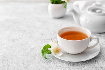 Fototapeta na wymiar Cup of jasmine tea, teapot and flowers on light background