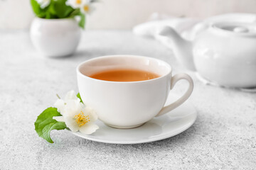 Cup of jasmine tea, teapot and flowers on light background