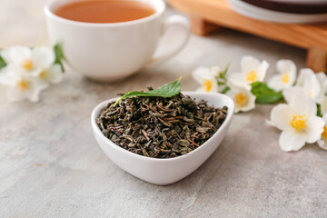 Bowl with dry green tea and cup of hot beverage on grunge background