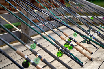 Many fishing rods on the wooden pier by the river or lake on a sunny day - Powered by Adobe