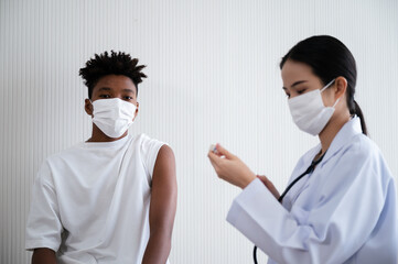 Female doctor or nurse preparing coronavirus 19 vaccination for African-American man waiting to be vaccinated in the laboratory. Concept of preventing the spread of COVID-19.