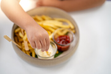 Little hand holding french fries at table.