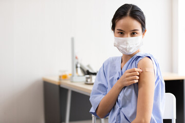 asian woman with medical mask, showing her arm after getting vaccinated, to build up or maintain immunity