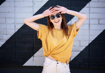 Portrait of a young happy girl woman in sunglasses and a yellow t-shirt on the street against a...