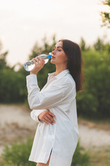 Girl drinks water from a plastic bottle.young caucasian woman in nature forest in woods while holding bottle of water