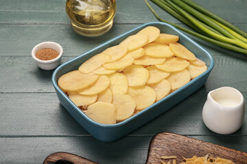 Preparing of tasty potato casserole in baking dish on color wooden background