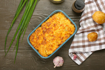 Baking dish with tasty potato casserole on wooden background