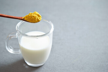A glass of milk and a spoonful of yellow powder