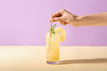 Female hand with glass of delicious cocktail on color background