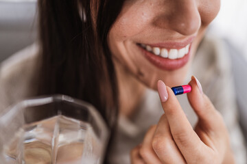 Close up of woman holding a capsule and glass of water. Taking vitamins, medications, and dietary supplements. The concept of disease prevention and treatment, healthcare concept.