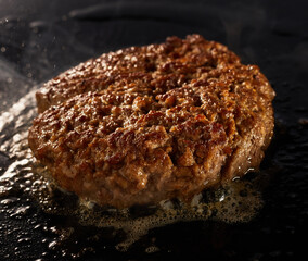 Ground beef burger grilling over a hot griddle