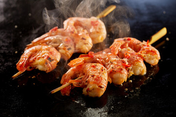 Tasty shrimps on skewers cooking on hot surface