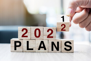 Businessman hand holding wooden cube with flip over block 2021 to 2022  Plans word on table background. Resolution, strategy, solution, goal, business and New Year holiday concepts