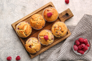 Board with tasty raspberry muffins on light background