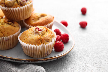 Plate with tasty raspberry muffins on light background, closeup