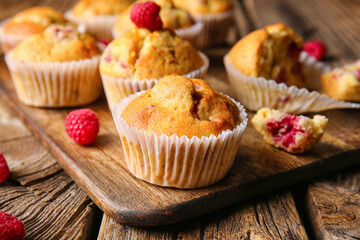Board with tasty raspberry muffins on wooden background, closeup