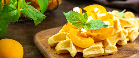 Traditional classic Belgian or Brussels waffles with apricots and almonds on a serving board on a brown wooden kitchen table closeup	