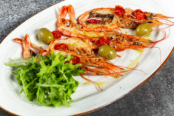 Fried langoustines served with olives and salad leaves. Grilled tasty langoustines on a white oval plate. Restaurant serving, horizontal orientation.