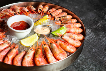Royal shrimp on ice. A plate with cold fresh prawns, ice, lemon, lime and sauce. Low key. Horizontal orientation.