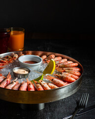 Royal shrimp on ice. A plate with cold fresh prawns, ice, lemon, lime and sauce. Sea buckthorne morse on the table. Low key. Vertical orientation.