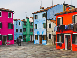 Fototapeta na wymiar Old peoples walking in the typical and very colorful streets of Burano. We see laundry being dried outside
