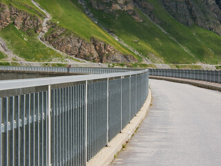 Fototapeta premium View of a single lane road in a curve, with railings at the roadside. Road on the embankment dam at Lac de Moiry reservoir, Switzerland. Focus on foreground, blur effect
