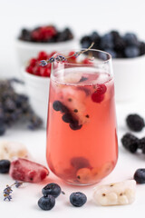 Fototapeta na wymiar Blurred image of a chilled fruit drink with ice and a sprig of lavender in the foreground, various berries in the background on a light background.Summer drinks.