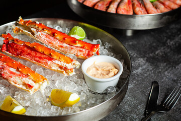 Phalanxes of red crab on ice. Lies on ice with lemon and lime and sauce. Restaurant serving. Low key, dark background with a dish of shrimps. Horizontal orientation