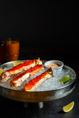 Phalanxes of red crab on ice. Lies on ice with lemon and lime and sauce. Restaurant serving. Low key, dark background with a glass of juice. Vertical orientation