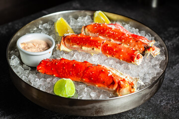 Phalanxes of red crab on ice. Lies on ice with lemon and lime and sauce. Restaurant serving. Low key, dark background, horizontal orientation