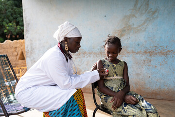 Black female doctor taking a small African schoolgirl's temperature with a digital thermometer during a home visit