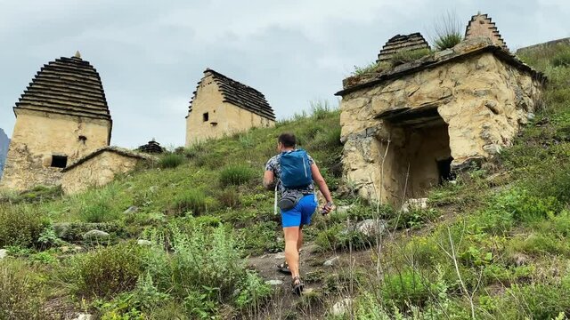 A tourist guy with a small backpack is walking along the ancient acropolis. Dargavs is the city of the dead. North Ossetia - Alania, Russia.