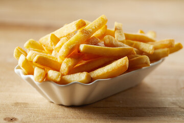 Tasty French fries in ceramic bowl on wooden surface